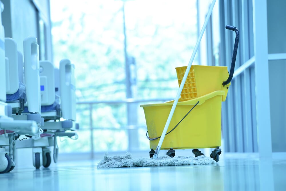 Mop and bucket in a bright, empty clinic corridor beside patient beds